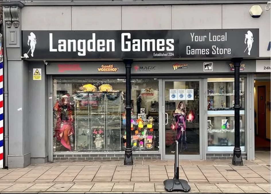Photo of the outside of Langden Games - shopfront with black fascia with the name of the shop, and plate glass windows with game decals on the window