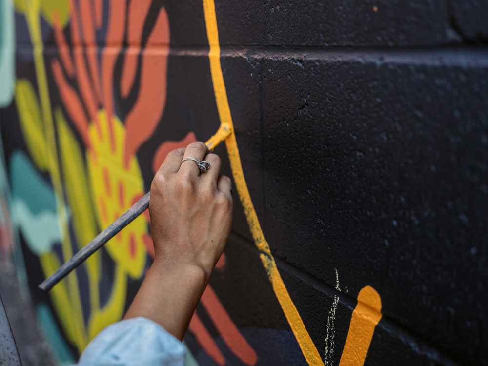 Photograph of someone's hand holding a paint brush and painting a mural on a wall